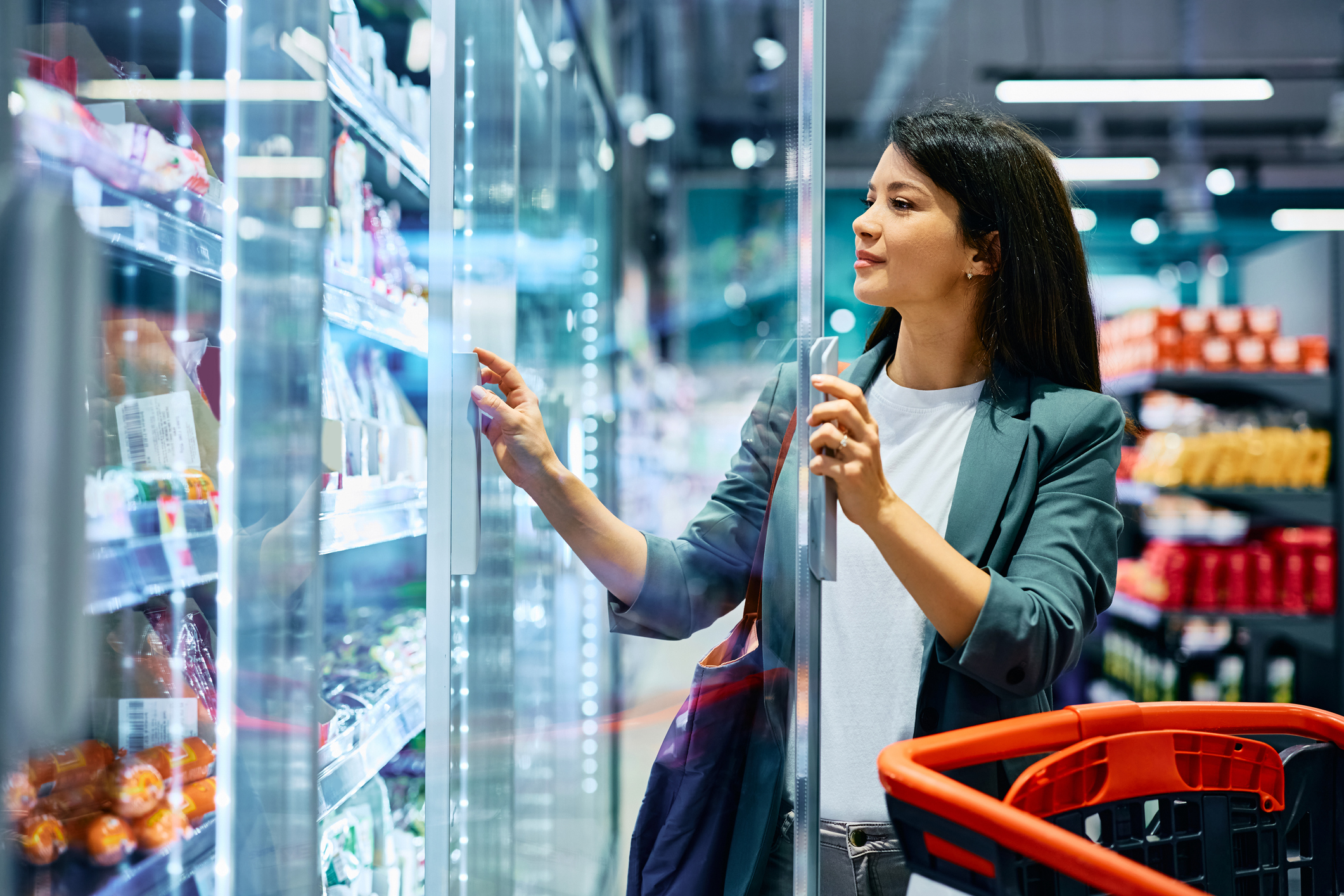 Smiling woman buying groceries at refrigerated section in a supermarket.